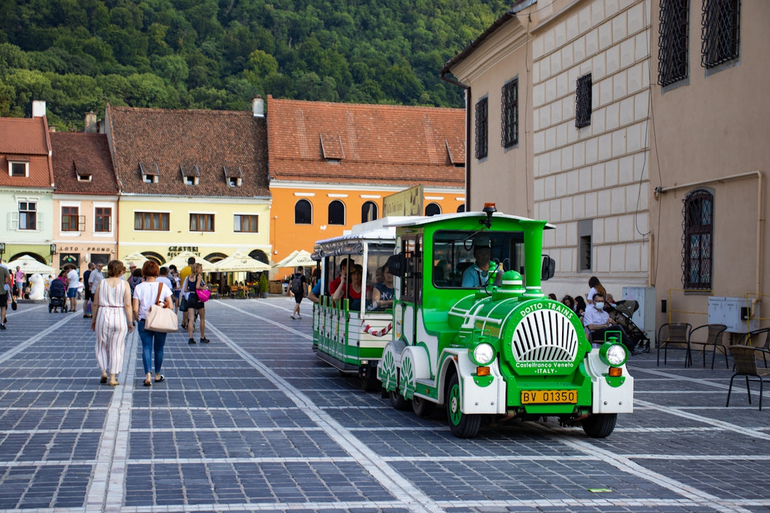 a green train traveling down a street next to tall buildings