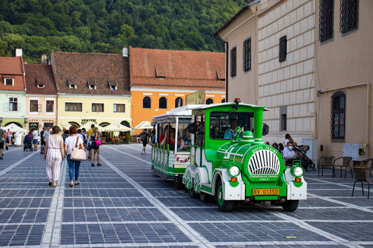 a green train traveling down a street next to tall buildings